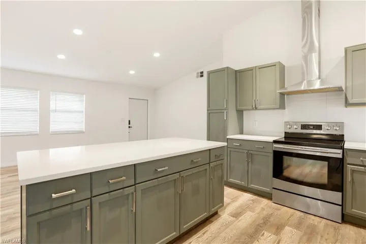 Kitchen with electric stove, island exhaust hood, light countertops, recessed lighting, and light wood-style floors
