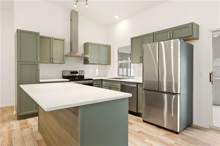 Kitchen featuring green cabinets, stainless steel appliances, a center island, light wood-style flooring, and lofted ceiling