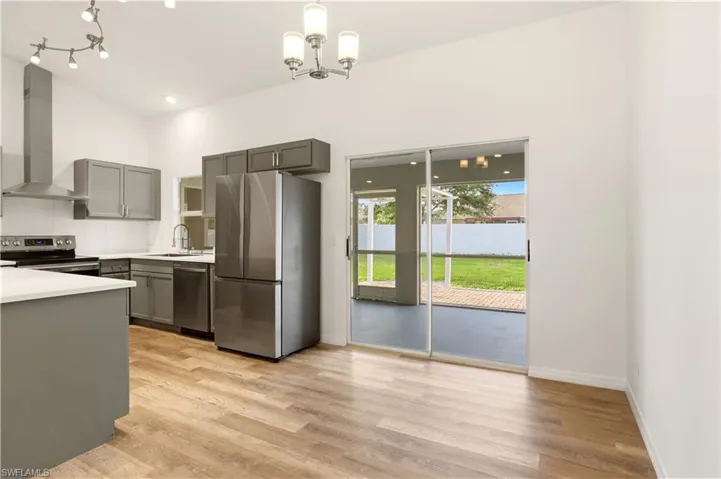 Kitchen with gray cabinetry, stainless steel appliances, light countertops, extractor fan, and light wood-type flooring