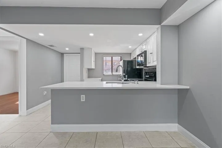 Kitchen with a sink, white cabinetry, a peninsula, black microwave, and light countertops