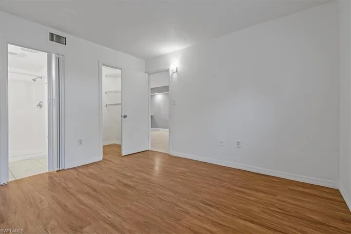 Unfurnished bedroom with a spacious closet, visible vents, baseboards, wood finished floors, and a closet