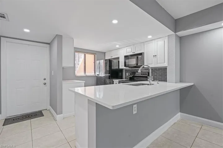 Kitchen featuring a peninsula, light tile patterned flooring, decorative backsplash, black appliances, and white cabinetry