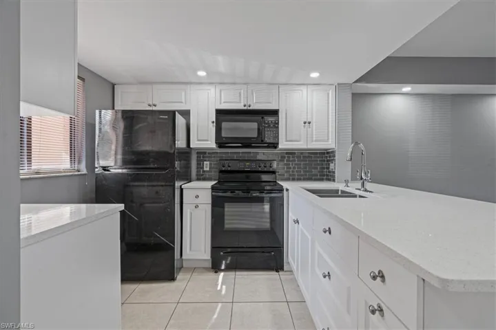 Kitchen with a peninsula, light tile patterned flooring, white cabinets, black appliances, and a sink