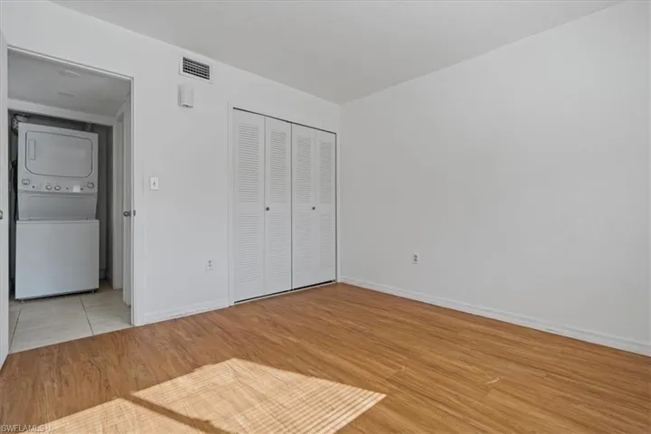 Unfurnished bedroom featuring light wood finished floors, stacked washer / dryer, baseboards, and visible vents