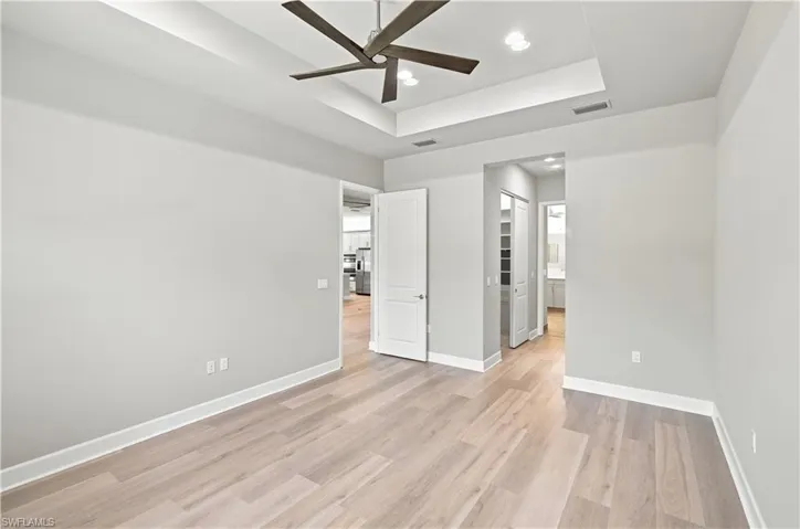 Spacious interior room featuring wood-finish flooring, a tray ceiling with recessed lighting, and a dark-toned ceiling fan