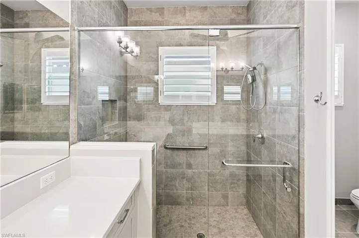 Primary Bathroom Spacious walk-in shower featuring a glass enclosure, grey-toned tile walls, and a mosaic pebble floor