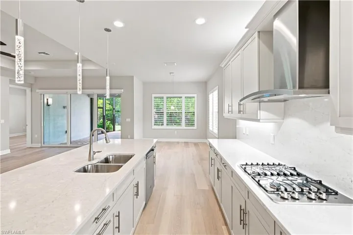 Modern kitchen featuring a large island with dual sinks, stainless steel appliances, a gas cooktop, light wood-finish flooring, and pendant lighting