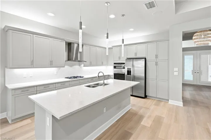 Contemporary kitchen featuring light gray cabinetry, stainless steel appliances, a large center island with a double sink, wood-finish flooring, and pendant lighting