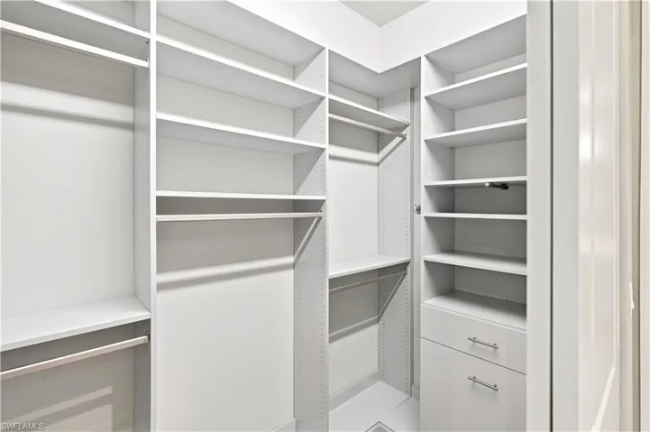 Built-in white custom closet system featuring multiple shelving units, integrated drawers with brushed nickel hardware, and multiple hanging rods