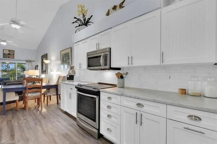 Kitchen with backsplash, appliances with stainless steel finishes, white cabinets, and light hardwood / wood-style floors