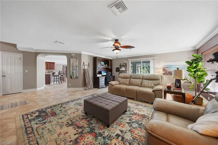 Tiled living room featuring ceiling fan, a textured ceiling, and ornamental molding