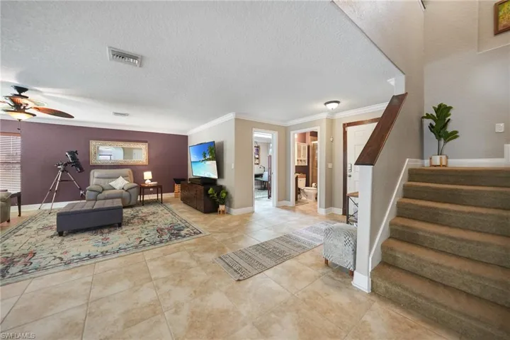 Tiled living room with a textured ceiling, ornamental molding, and ceiling fan