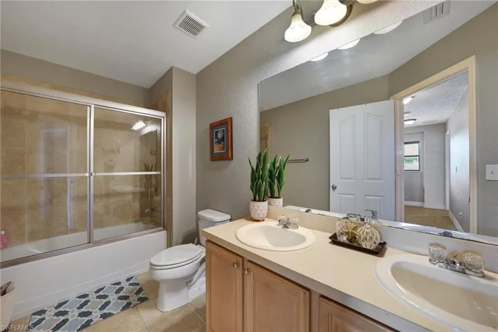 Full bathroom featuring vanity, a textured ceiling, bath / shower combo with glass door, tile patterned floors, and toilet