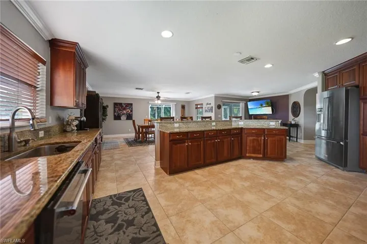 Kitchen featuring light stone counters, sink, kitchen peninsula, stainless steel appliances, and ornamental molding
