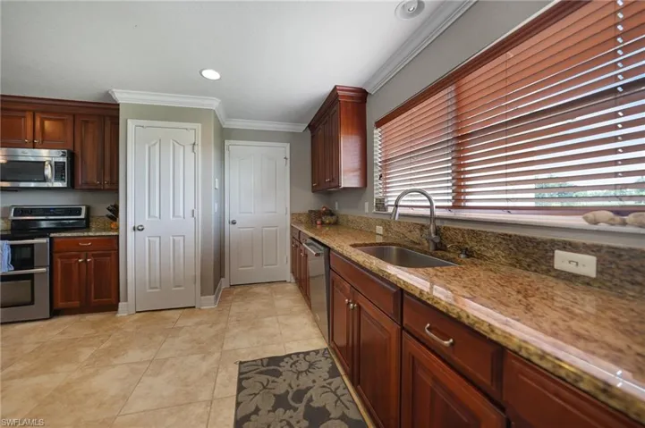 Kitchen featuring light tile patterned flooring, ornamental molding, sink, stainless steel appliances, and light stone countertops
