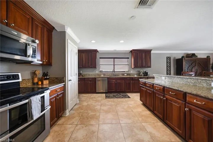 Kitchen with appliances with stainless steel finishes, dark stone countertops, light tile patterned floors, crown molding, and sink
