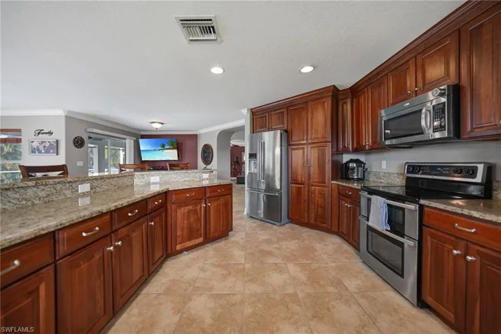 Kitchen featuring light stone countertops, appliances with stainless steel finishes, crown molding, and light tile patterned floors