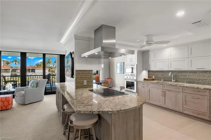 Kitchen with sink, wall chimney exhaust hood, black electric stovetop, backsplash, and light brown cabinetry