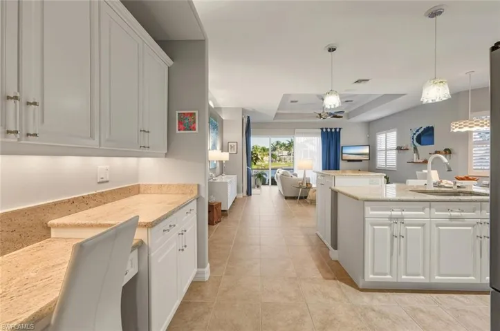 Kitchen featuring white cabinets, hanging light fixtures, light stone counters, open floor plan, and a raised ceiling