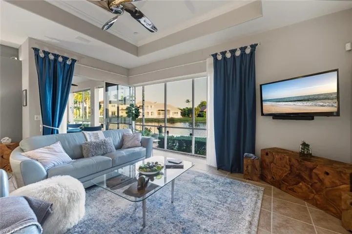 Living room featuring light tile patterned floors, ceiling fan, a raised ceiling, and crown molding