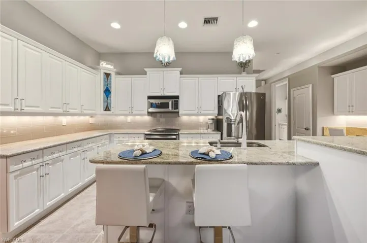 Kitchen featuring white cabinetry, stainless steel appliances, light stone counters, decorative light fixtures, and recessed lighting