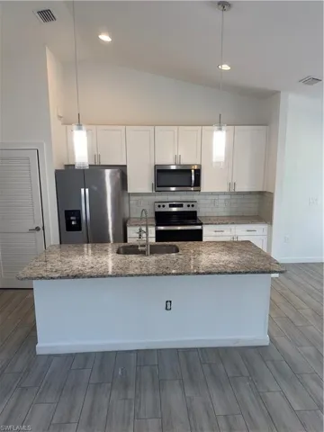 Kitchen featuring stainless steel appliances, tasteful backsplash, white cabinets, dark stone counters, and lofted ceiling