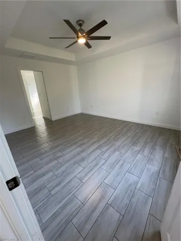 Empty room with a tray ceiling, wood tiled floors, and ceiling fan