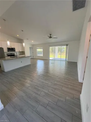Unfurnished living room with wood finish floors, vaulted ceiling, ceiling fan, and recessed lighting