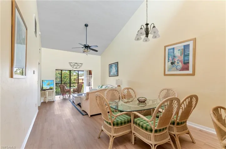 Dining area featuring light wood-type flooring, ceiling fan with notable chandelier, and high vaulted ceiling