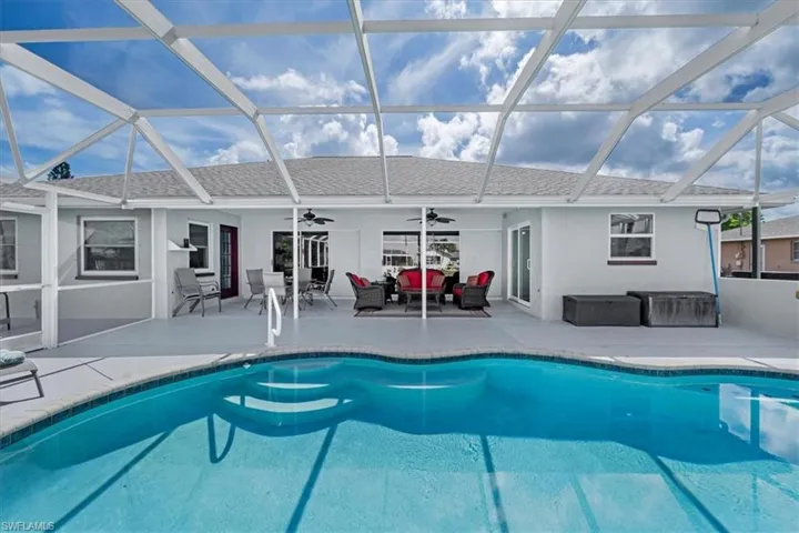 Screened lanai featuring a freeform swimming pool with integrated steps, a spacious concrete patio, multiple sliding glass doors, and a covered porch area with ceiling fans