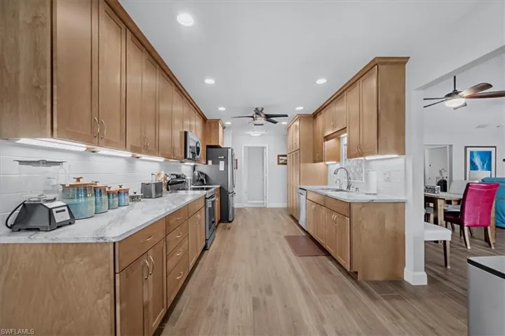 Galley kitchen featuring extensive light wood-finish cabinetry, light-toned countertops, a white subway tile backsplash, recessed lighting, and wood look tile flooring