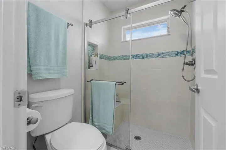 Modern shower enclosure featuring a sliding glass door, white rectangular tile surround, and a mosaic accent band