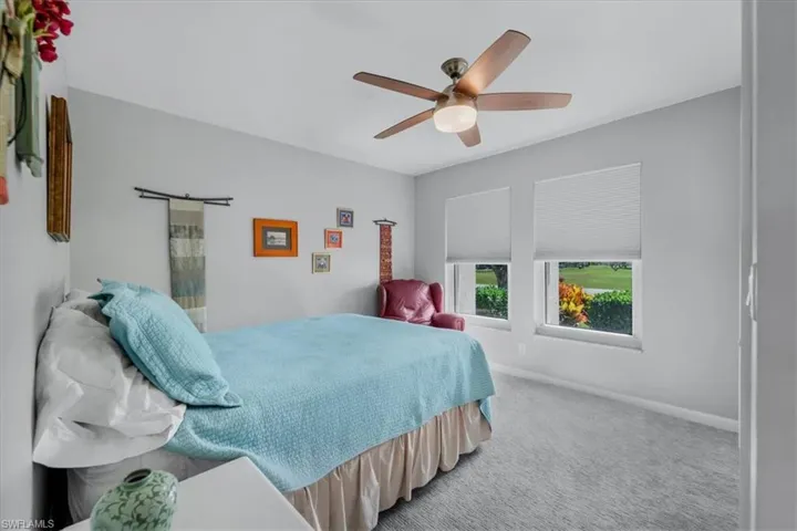 Neutral-toned bedroom featuring twin windows with integrated blinds, a ceiling fan with light fixture, light gray walls, and carpet flooring
