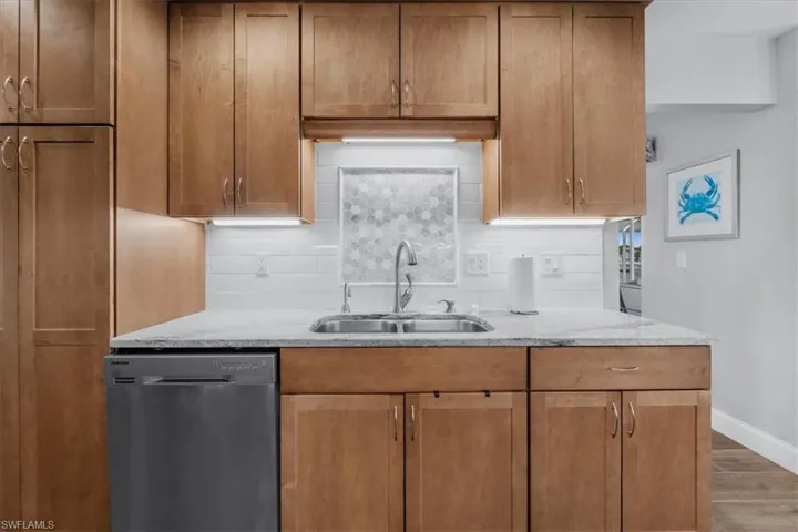 Kitchen featuring light wood-finish cabinetry, under-cabinet lighting, stainless steel sink with a gooseneck faucet, light-toned countertop, and a white subway tile backsplash with a hexagonal accent panel
