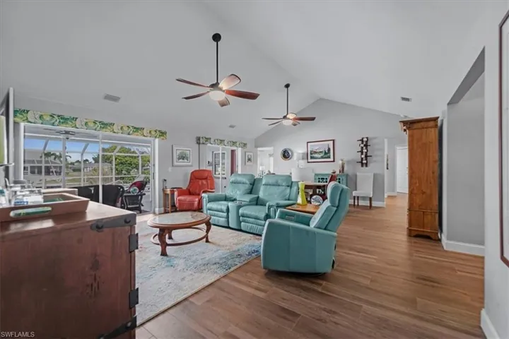 Spacious living area featuring vaulted ceilings, wood look Tile flooring, and multiple ceiling fans