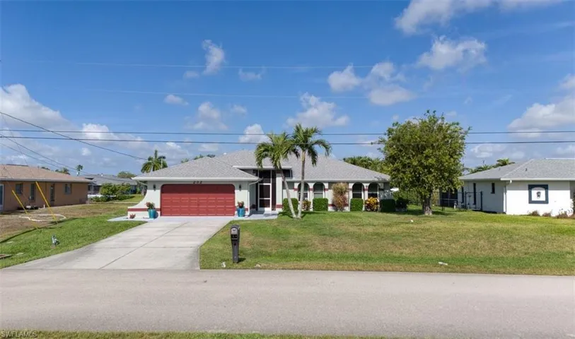Single-story residence featuring a red garage door, concrete driveway, and mature landscaping