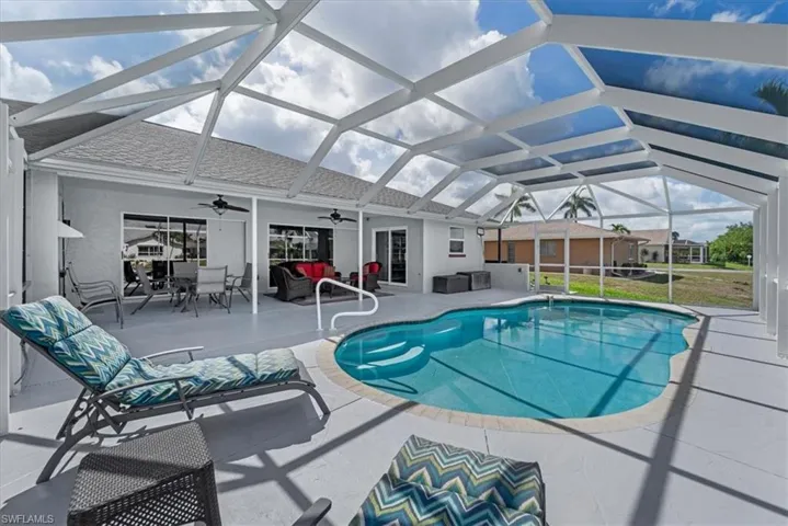 Screen-enclosed pool area featuring a freeform pool with integrated steps, a spacious painted concrete deck, a covered patio with recessed lighting, and multiple sliding glass door entries