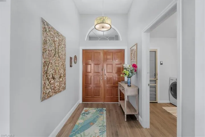 Foyer featuring double entry doors with a transom window, high ceilings, wood-finish flooring, and a decorative drum pendant light fixture