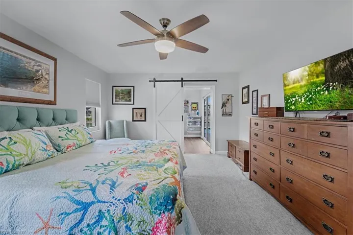 Carpeted bedroom featuring a ceiling fan with light, a white barn door, and a built-in closet with shelving