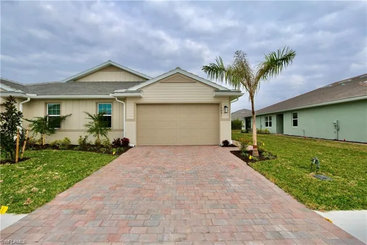 Ranch-style home featuring a front lawn, decorative driveway, a garage, and board and batten siding