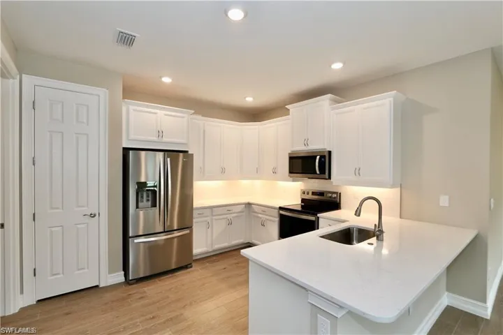 Kitchen featuring stainless steel appliances, white cabinets, light wood finished floors, decorative backsplash, and recessed lighting