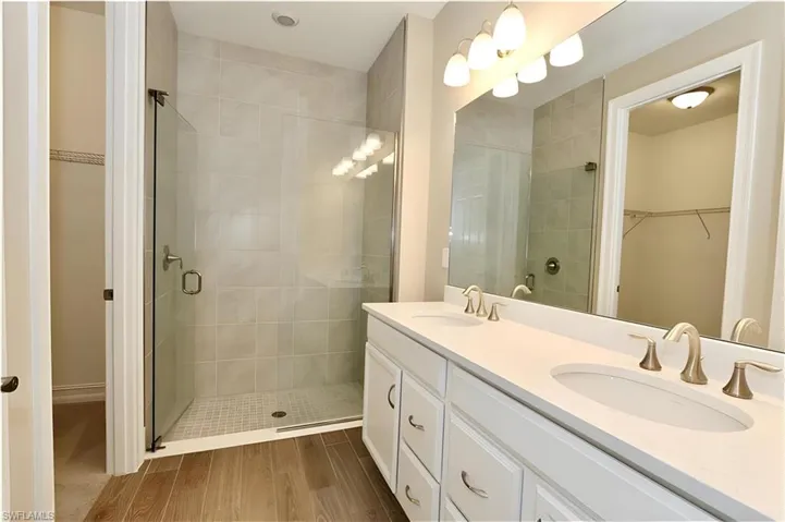 Full bath with a walk in closet, double vanity, wood finish floors, and a shower stall