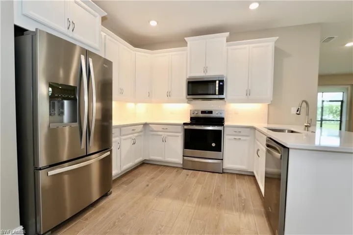 Kitchen featuring appliances with stainless steel finishes, white cabinetry, light wood-type flooring, a peninsula, and decorative backsplash
