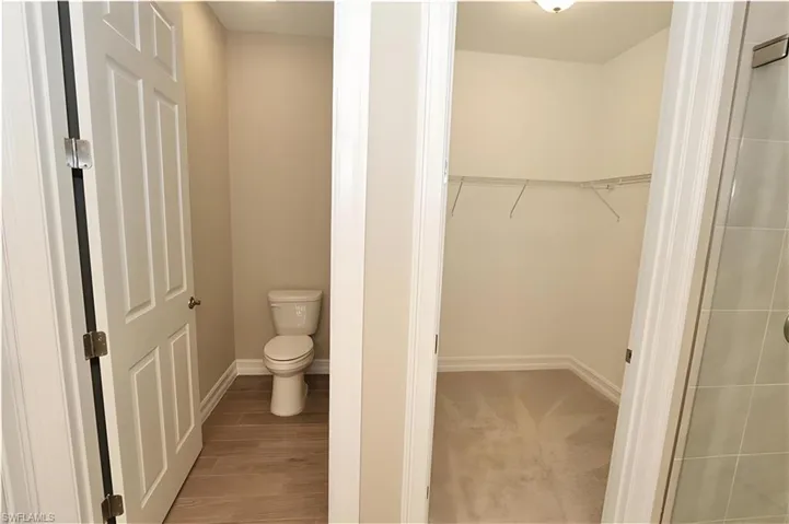 Full bath with a spacious closet, wood finish floors, and a stall shower