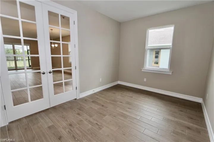 Unfurnished room featuring french doors, light wood-type flooring, a chandelier, and plenty of natural light