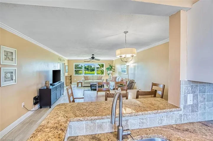 Kitchen with ornamental molding, a textured ceiling, ceiling fan, light wood-type flooring, and light stone counters