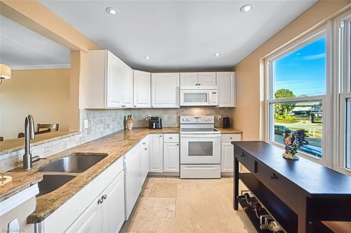 Kitchen with white appliances, white cabinetry, light stone counters, backsplash, and recessed lighting