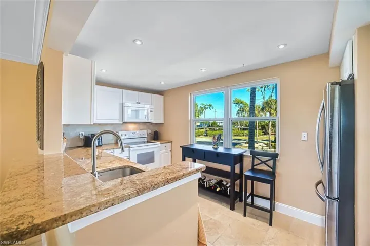 Kitchen featuring white appliances, light stone counters, white cabinets, tasteful backsplash, and recessed lighting