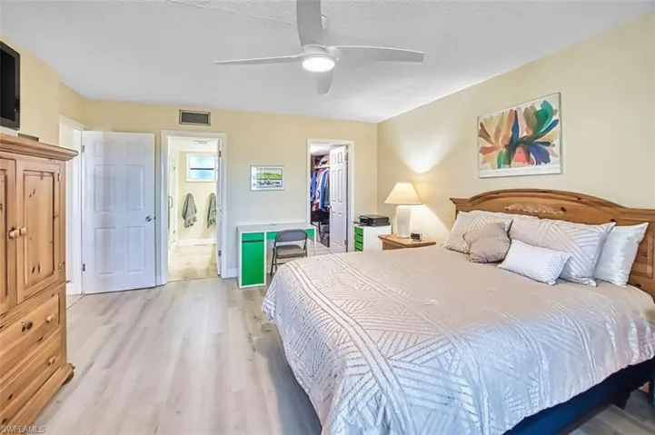 Master Bedroom with light wood-style floors, a walk in closet, a ceiling fan, and a textured ceiling