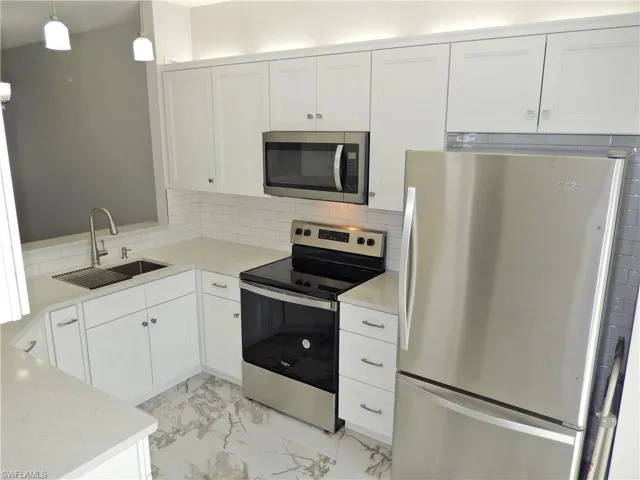 Kitchen with tasteful backsplash, stainless steel appliances, hanging light fixtures, sink, and white cabinets